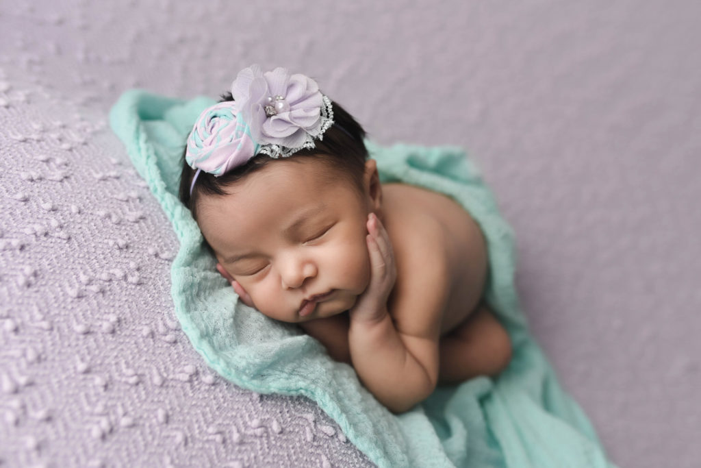 Newborn baby girl by Ashli Unkart Photography, sleeping on a purple and teal set.