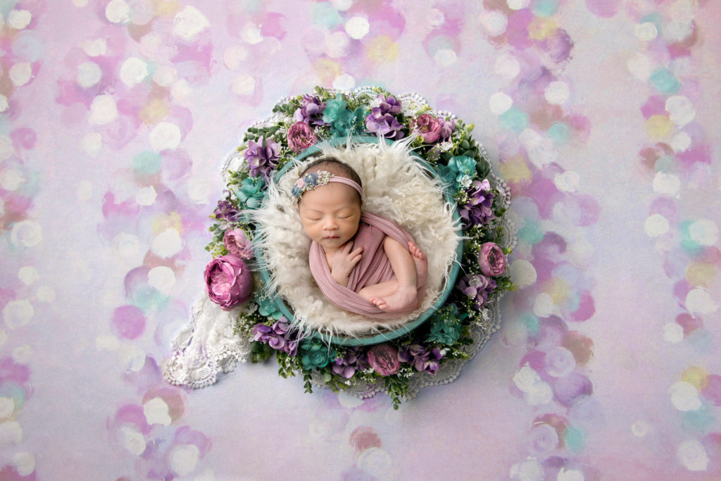 Newborn baby girl in a bowl surrounded by flowers, by Crystal Lee Photography.